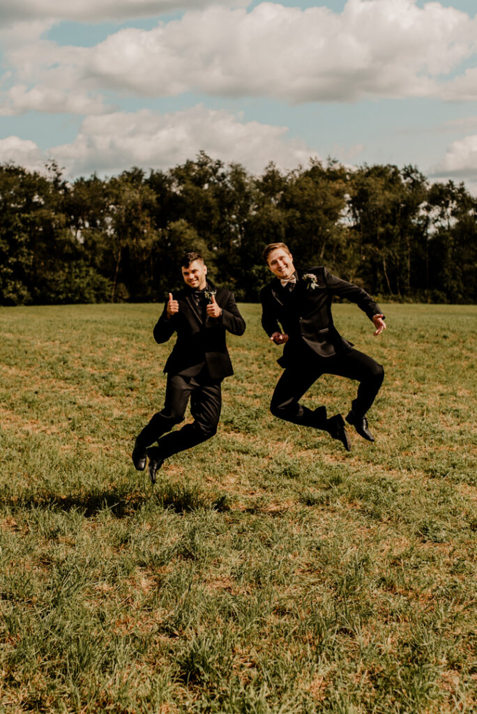 Groom and one of his groomsmen jumping in the air, touching their feet together. 