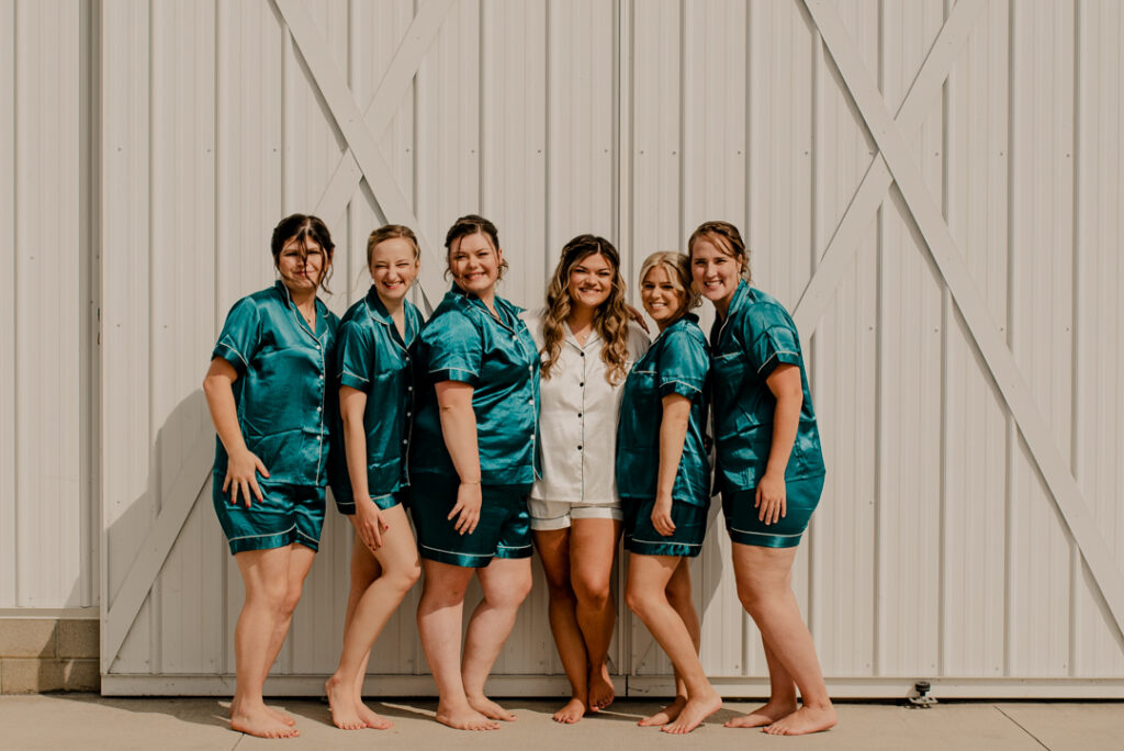 Bride with her bridesmaids smiling at the camera. They are wearing there getting ready PJ's 