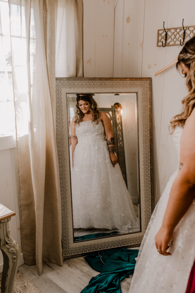 Bride putting on her dress fully, looking at herself in the mirror. 