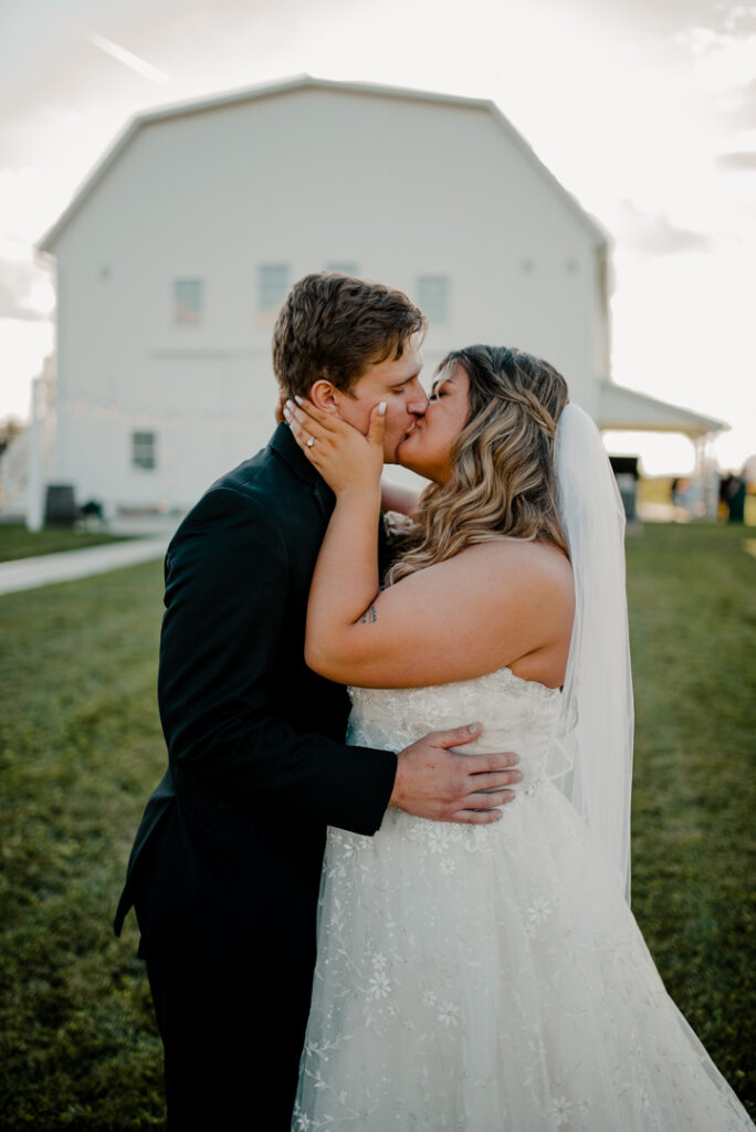 Close up of bride and groom kissing. The barn behind them. Bride is touching grooms face. 