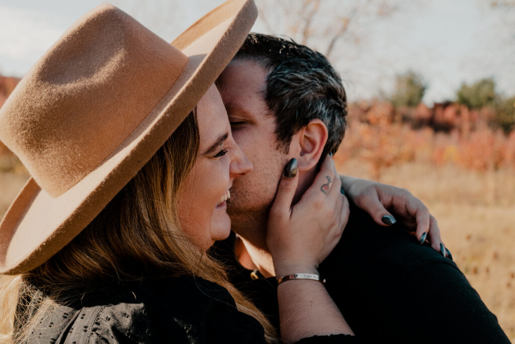 Close up of man and woman faces and he is kissing her cheek and she is holding his face. 