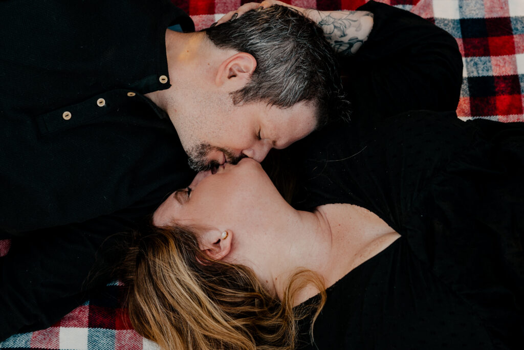 Man and woman both laying on their backs, kissing each other. Shot from above. 